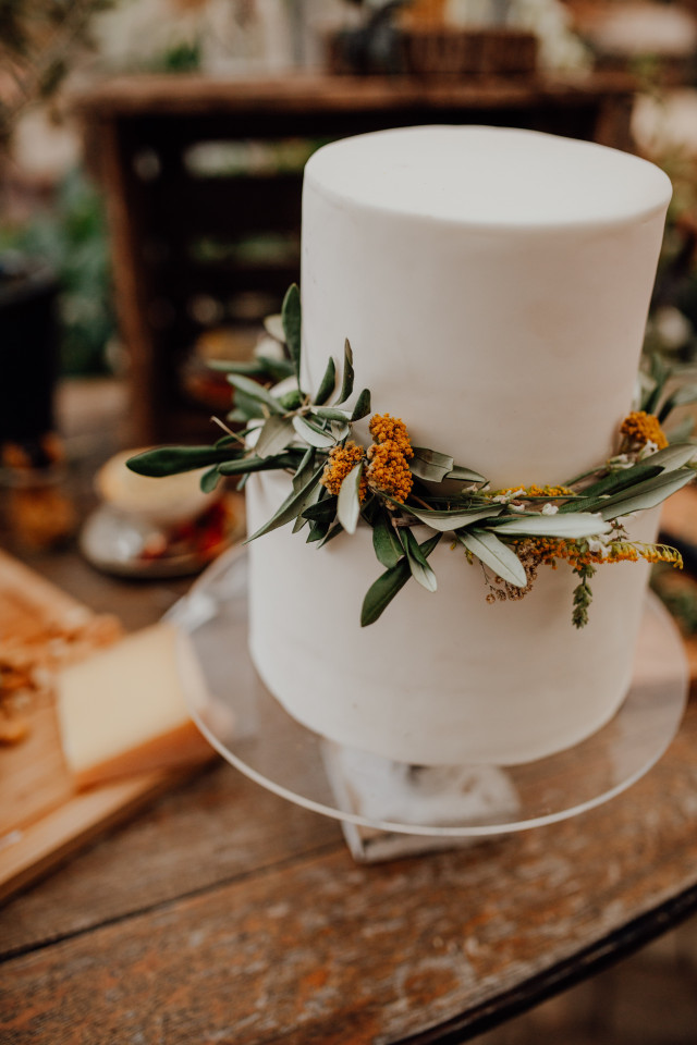 Zweistöckige Hochzeitstorte mit weißem Fondant und grünen Zweigen als Dekoration