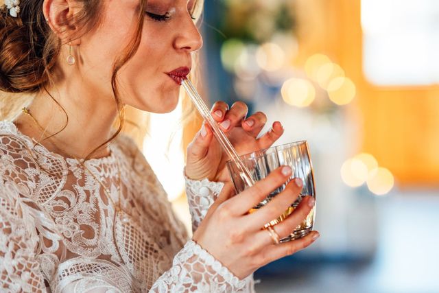 Braut trinkt aus einem Glas mit Glasstrohhalm