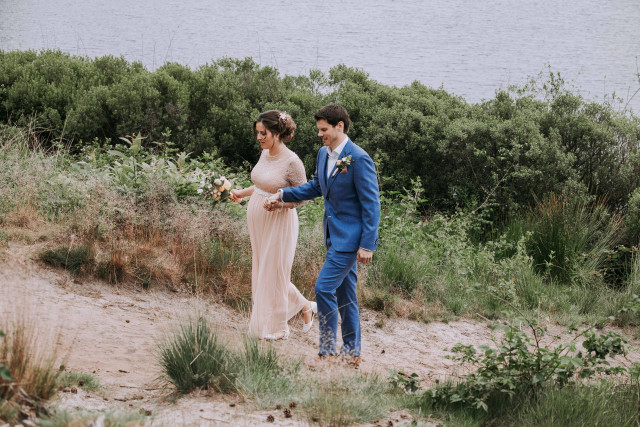 Groom in a light suit and bride walking along a coastal path