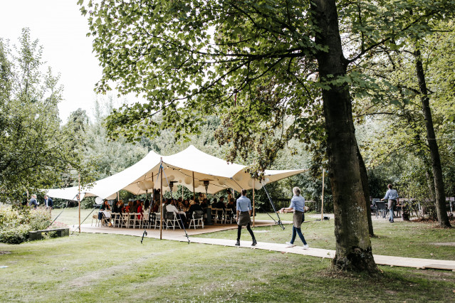 Elegante stretchtent opgezet in een weelderige tuin voor de bruiloftsreceptie, met gasten die rondlopen op het gazon.