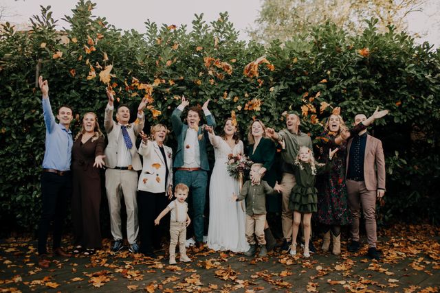 bruidspaar staat met familie tussen de herfstbalderen