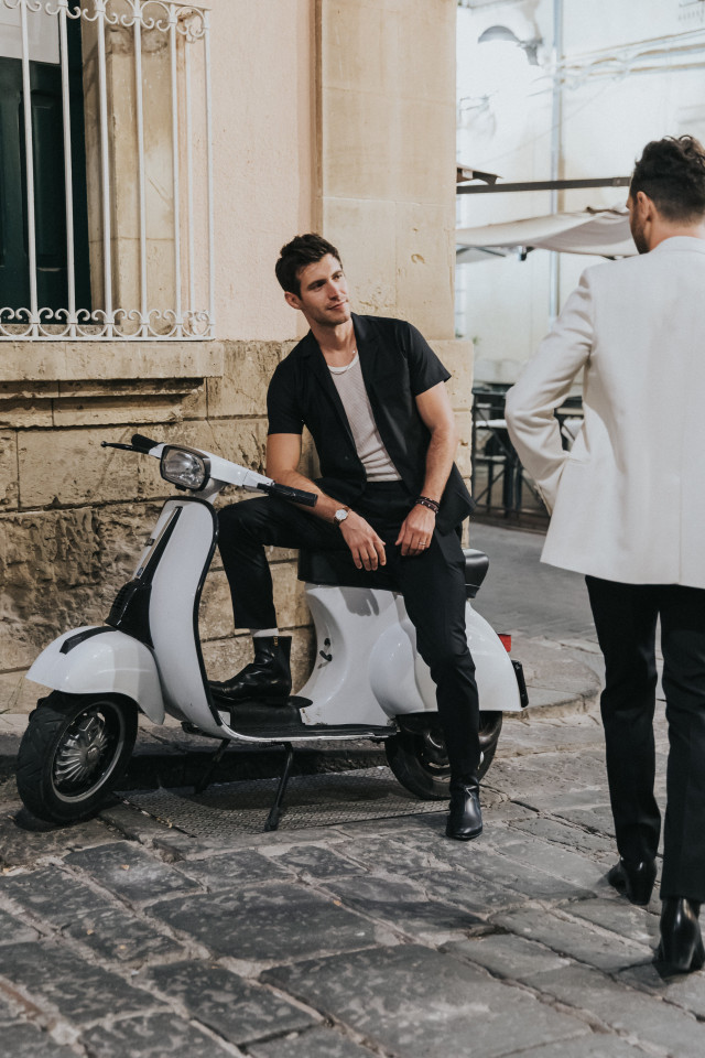 A man on a white Vespa waits as the celebration carries on.