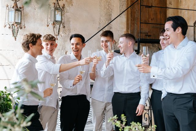 A group of men in white shirts toast with champagne glasses at a wedding.
