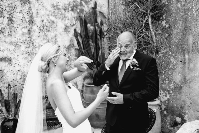 Black and white photo of a bride laughing with her father as he wipes away a tear during their first look.