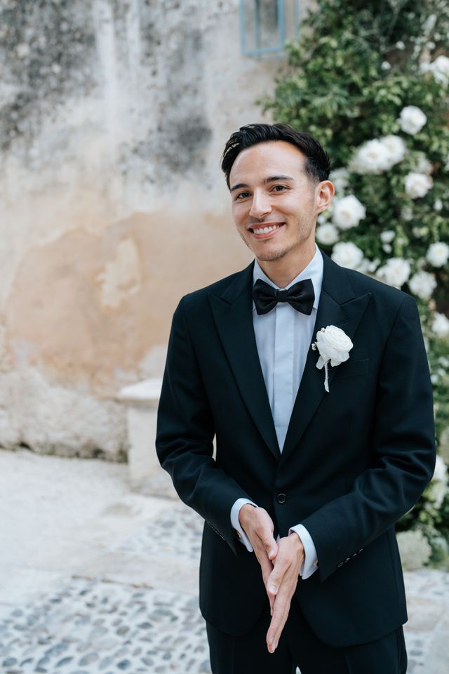 A portrait of the smiling groom in a tuxedo with a boutonniere on his lapel.
