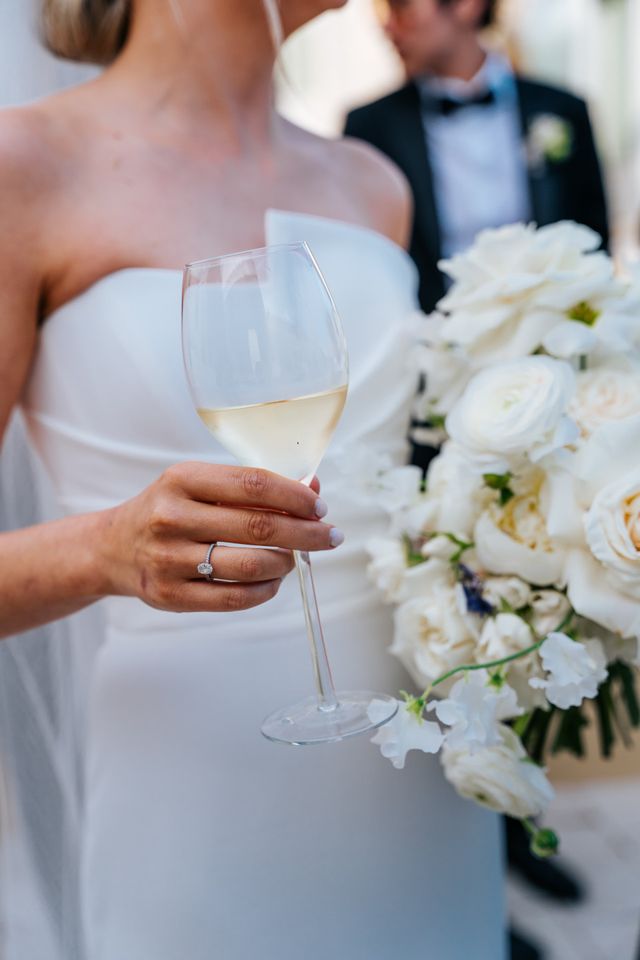 A detail of the bride with her engagement ring holding a glass of white wine.
