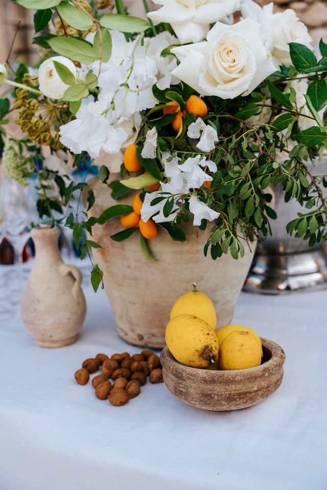 Detail of a rustic floral arrangement with white roses, kumquats, and a dish of lemons.