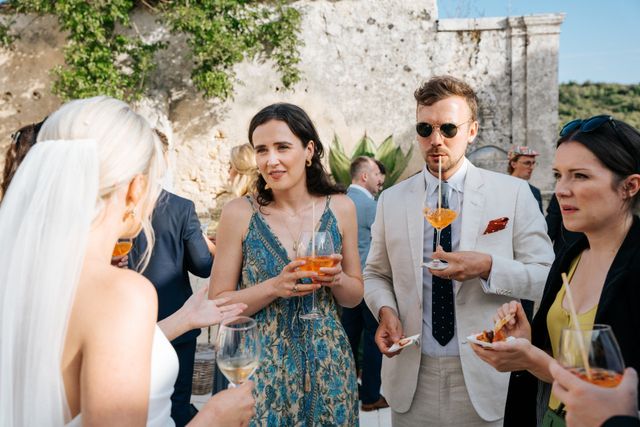 Guests holding Aperol spritzes chat together during cocktail hour.