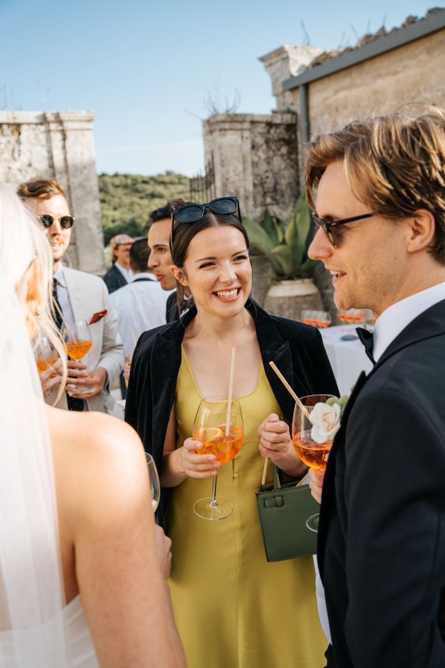 Laughing guests hold Aperol spritzes as they chat at the reception.