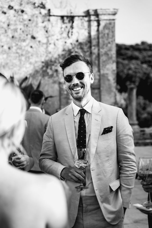 A black and white photo of a laughing male guest in sunglasses.