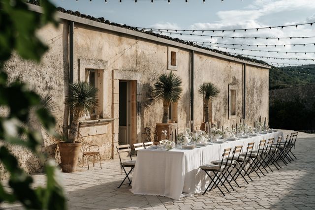 A long, elegantly set dinner table runs alongside a weathered facade at the reception.