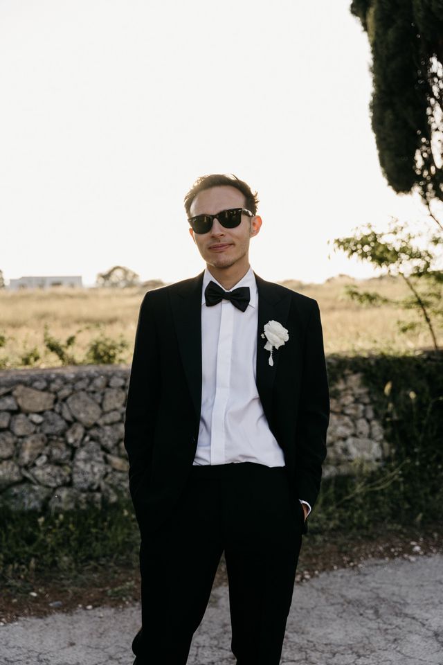 A groom in a black tuxedo with sunglasses and a white boutonniere.