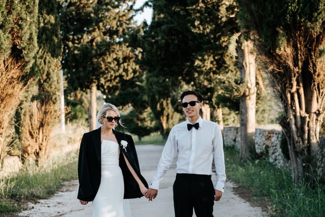 The couple walks hand in hand wearing sunglasses on a sunny day.