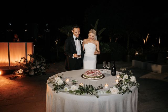 The couple cuts their wedding cake together at a sunlit Mediterranean venue.