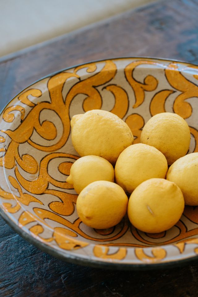 A still life of yellow lemons on a yellow Mediterranean dish at the table.
