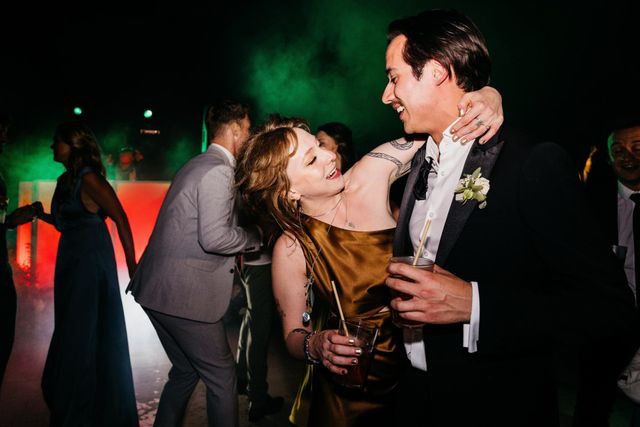 A laughing woman dances with her arm around a partner on the dance floor.