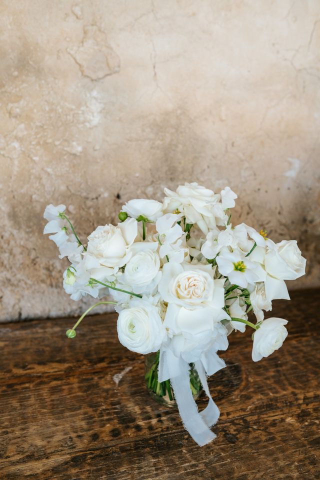 A simple white bridal bouquet of roses and fine flowers with ribbons resting on wood.