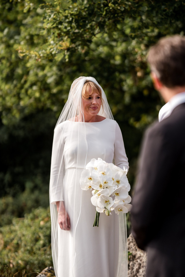 Braut trägt schlichtes Brautkleid, langen Schleier und Orchideen als Brautstrauß