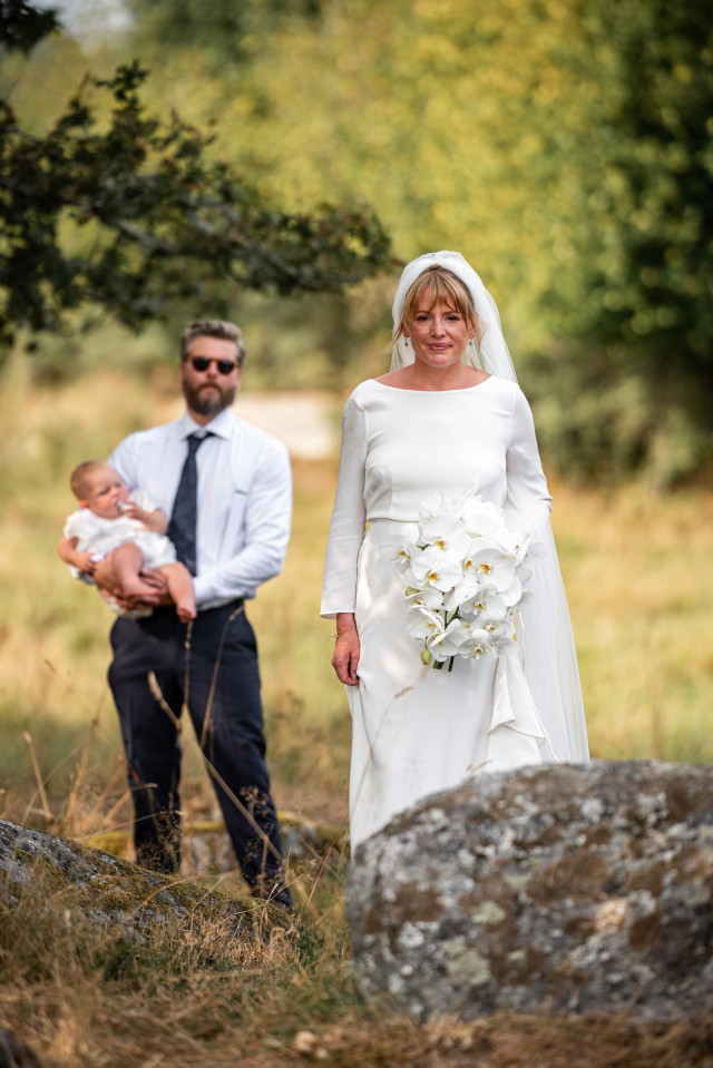 Braut und Bräutigam mit Baby stehen auf einer Wiese