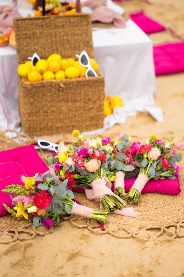 Bunte Blumensträuße liegen am Strand neben einem großen Korb mit Zitronen