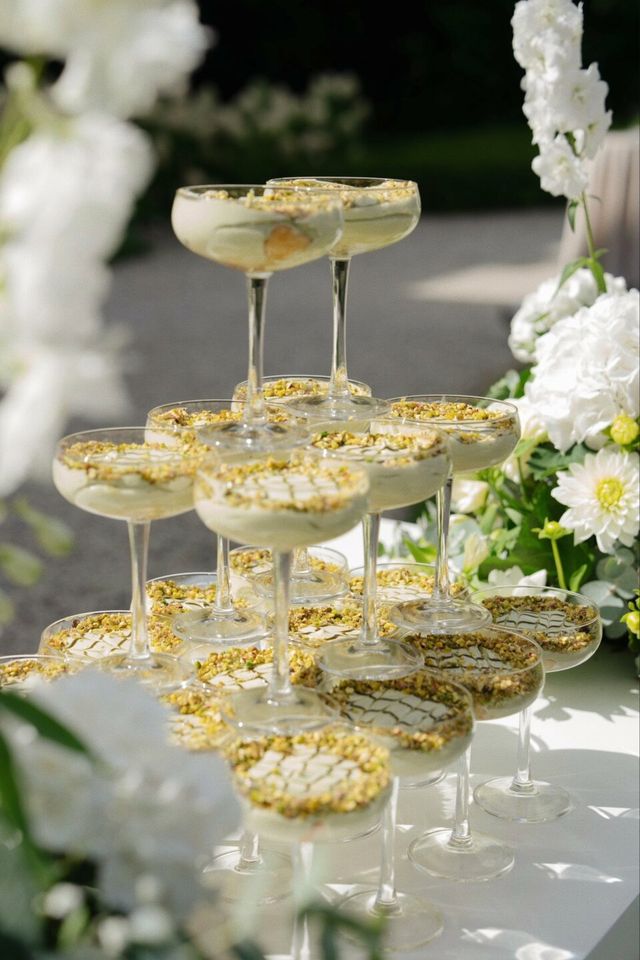 Champagne tower of gold-rimmed coupe glasses framed by white flowers