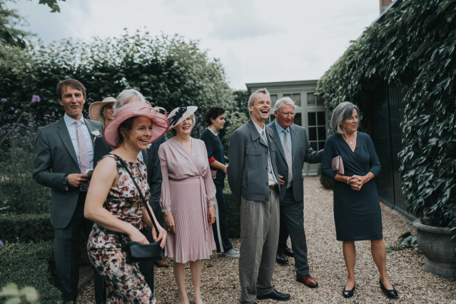 A group of festively dressed guests in hats stands together on the grass.