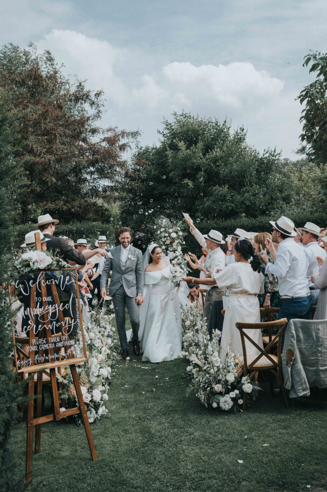 The couple walks hand in hand through a lush floral arch after the ceremony.