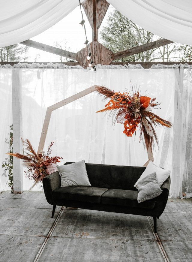 Couch mit orange-braunen Trockenblumen unter weißem Zelt