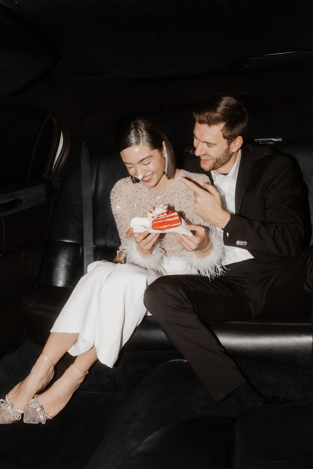 Brautpaar sitzt in der limousine und isst Hochzeitstorte, Bräutigam schmiert scherzhaft Kuchen auf die Nase der Braut  