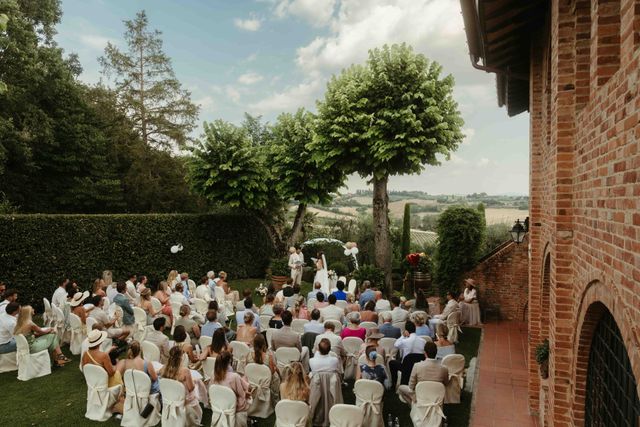 An outdoor wedding ceremony with guests seated in the garden of a Tuscan villa, surrounded by lush greenery.