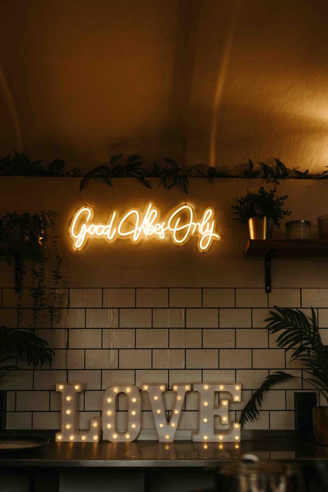 A neon Good Vibes Only sign glows above illuminated LOVE marquee letters in a warmly lit venue.