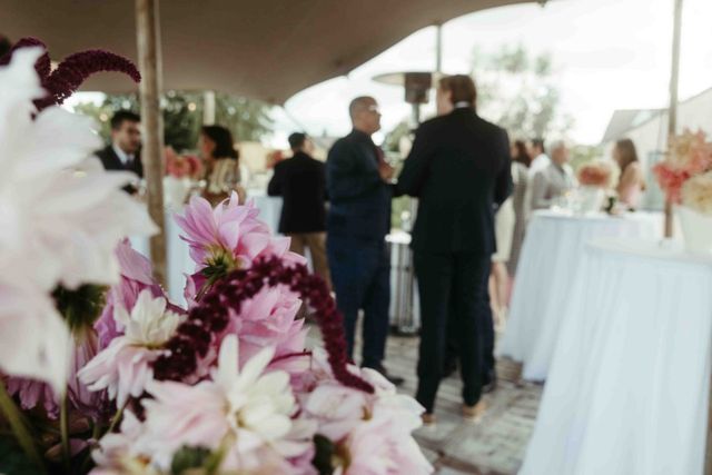 Invités de mariage discutant sous une tente lors d'une réception en extérieur, fleurs colorées au premier plan