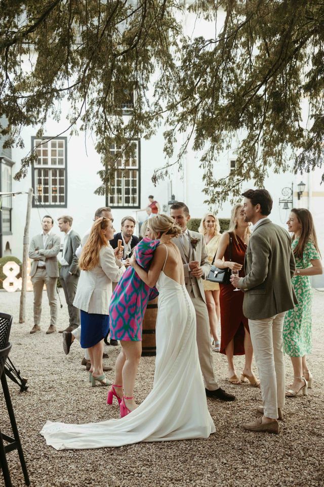 The bride in her white gown embraces a guest in a printed dress in the courtyard as other guests mingle.
