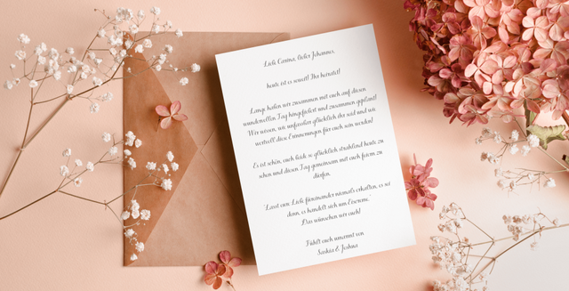 Hochzeitskarte liegt neben rosa Blumen auf einem rosa Untergrund