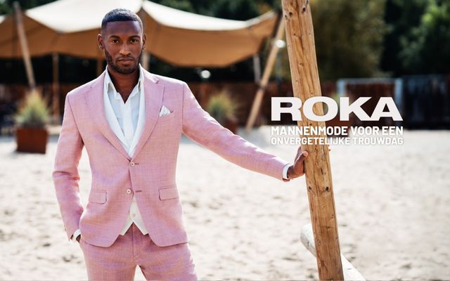 een man in een roze pak die naast een houten hek staat