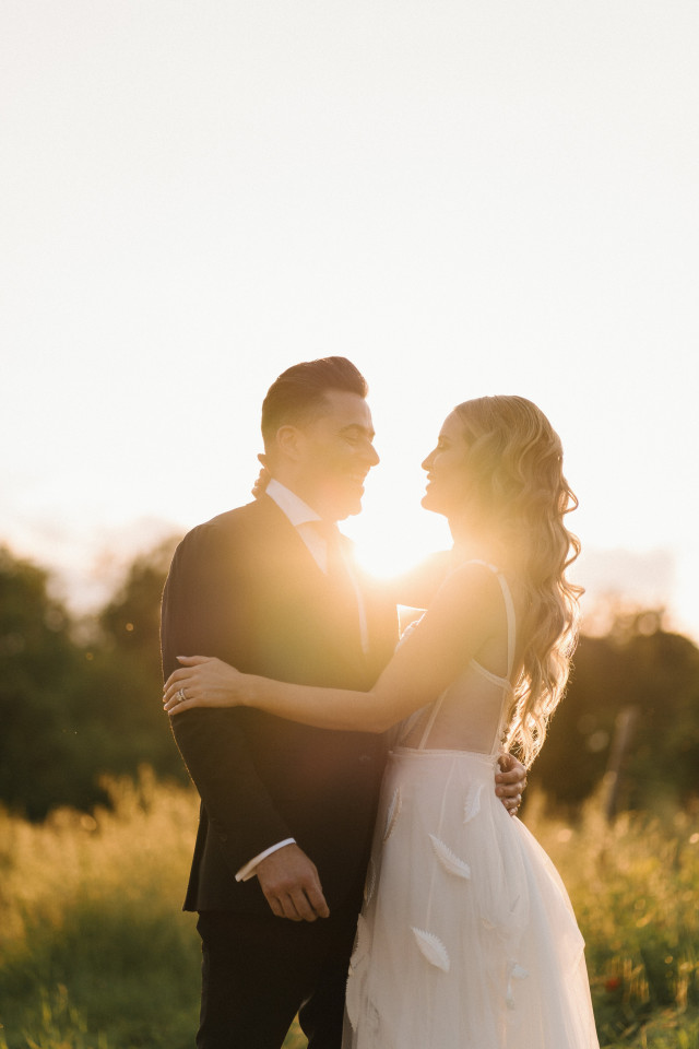 A couple embrace in a golden field at sunset, the sun glowing warmly between them.