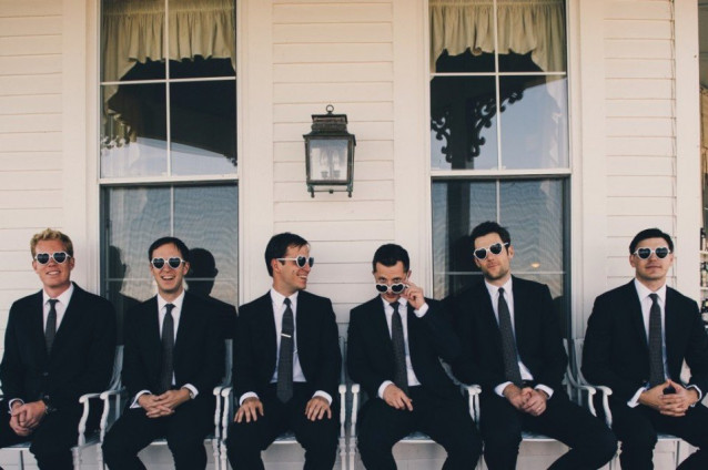 Groomsmen sitzen auf einer Bank und tragen schwarze Anzüge