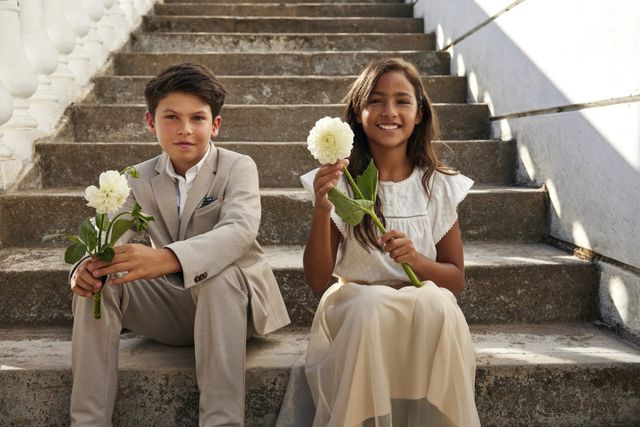 Junge und Mädchen sitzen auf einer Steintreppe in Hochzeitsoutfits