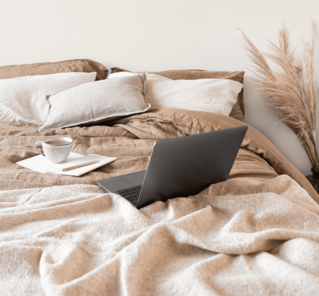 Laptop auf Bett mit Leinenbettwäsche und Kissen