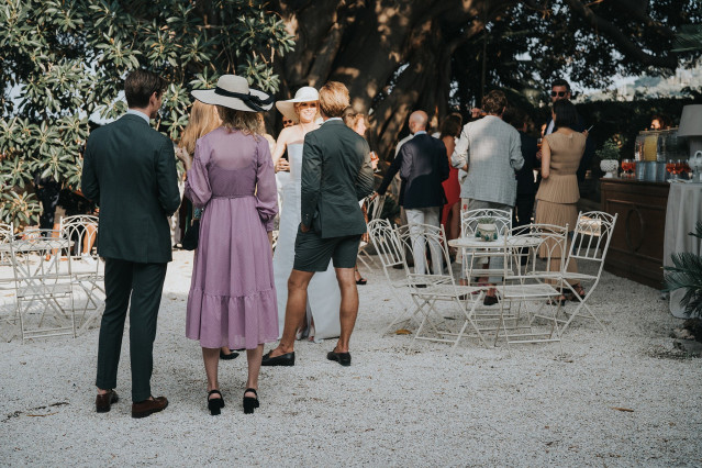 Guests in hats chat by small white cocktail tables at the wedding.