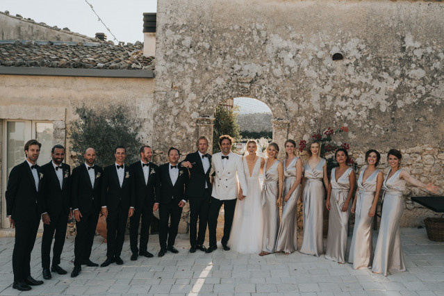 A formal group photo of the couple with bridesmaids and men in tuxedos.