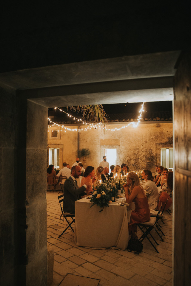 Guests dine at a long table dressed with floral arrangements and candlelight.