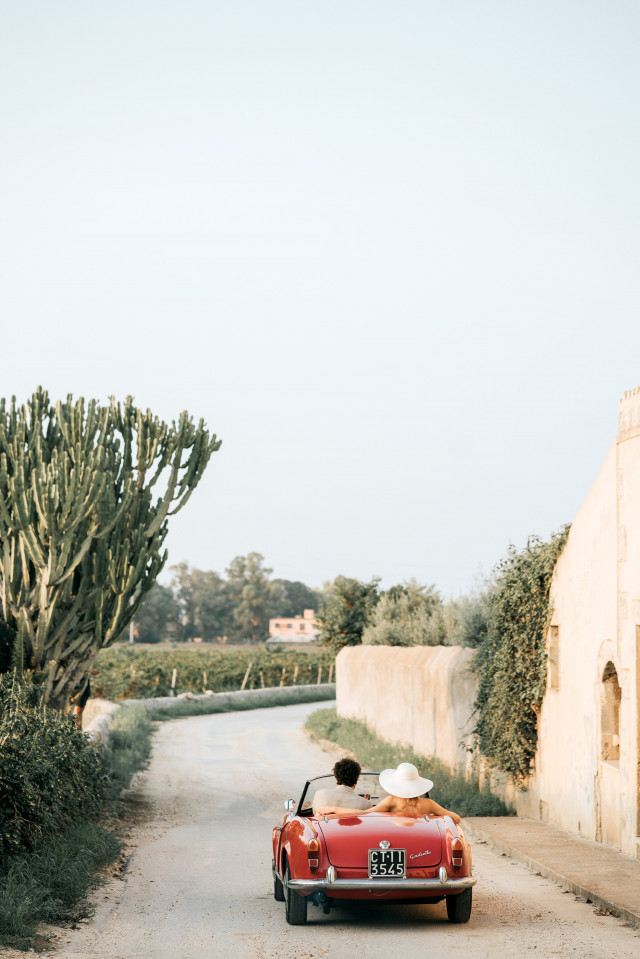 A red convertible carries the couple away down a sandy road lined with cacti.