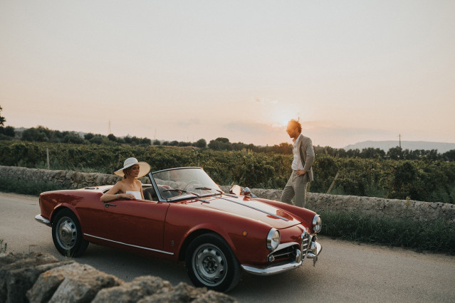 A red classic convertible parked along a country road near the wedding.