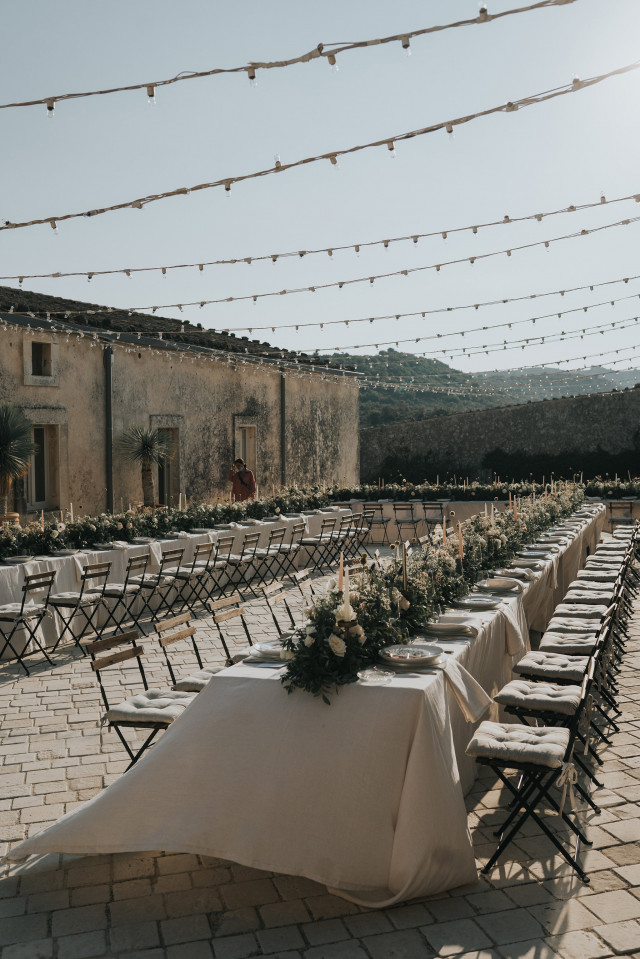 Long festively set tables with floral centerpieces on a terrace.