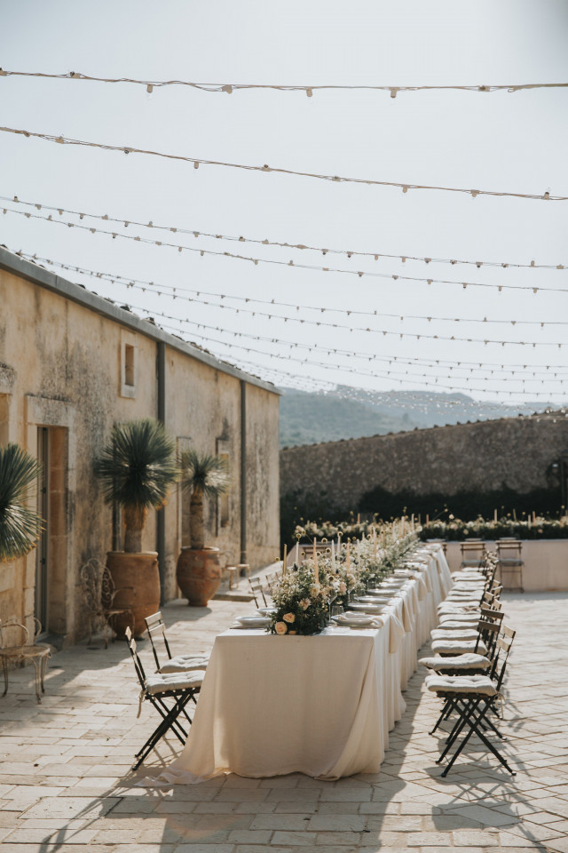 A long set dinner table on a Mediterranean terrace dressed with flowers.