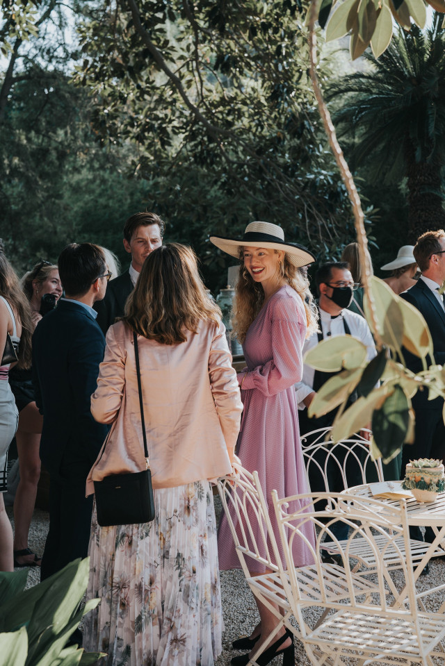 Laughing guests, including a woman in a pink hat, enjoy the gathering.