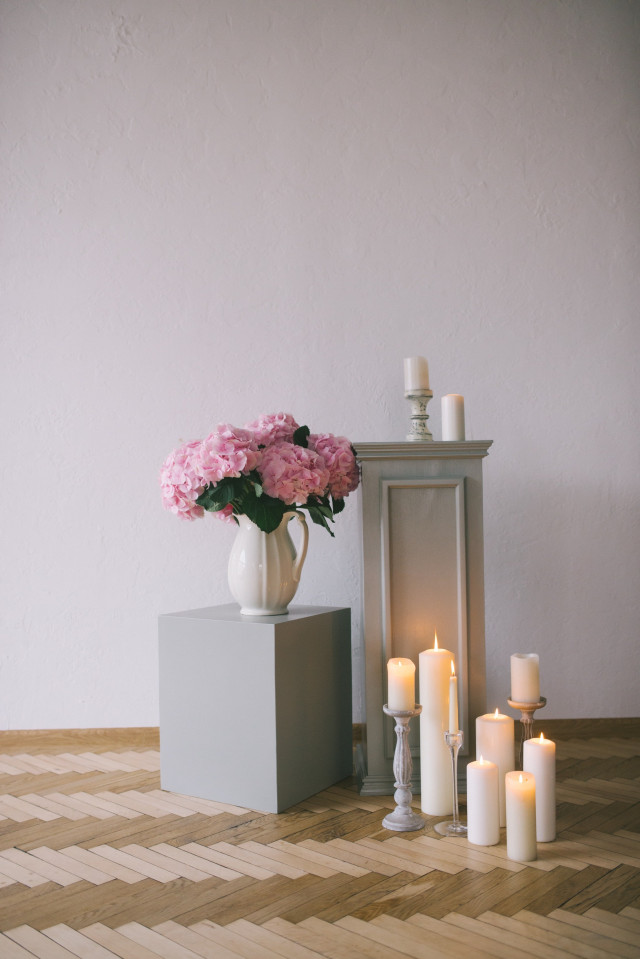 Kerzen vor pinken Blumen und Steinwand