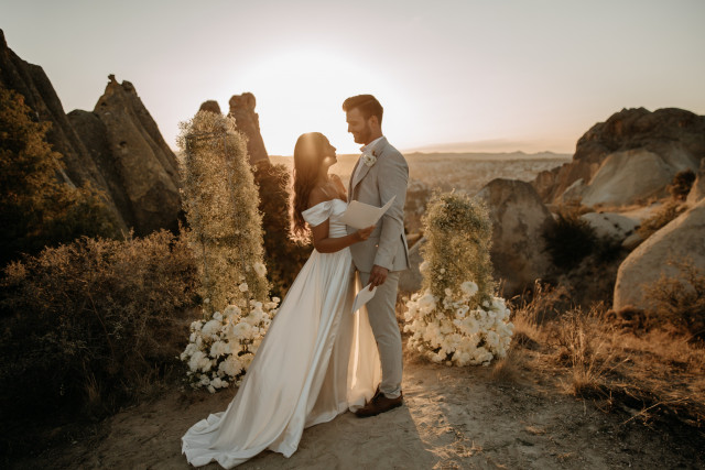 Braut und Bräutigam stehen vor einer Klippe mit Sonnenuntergang im Hintergrund