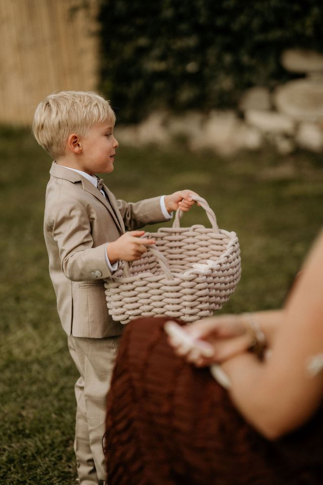 Young ring bearer in a beige suit carrying a basket at the ceremony